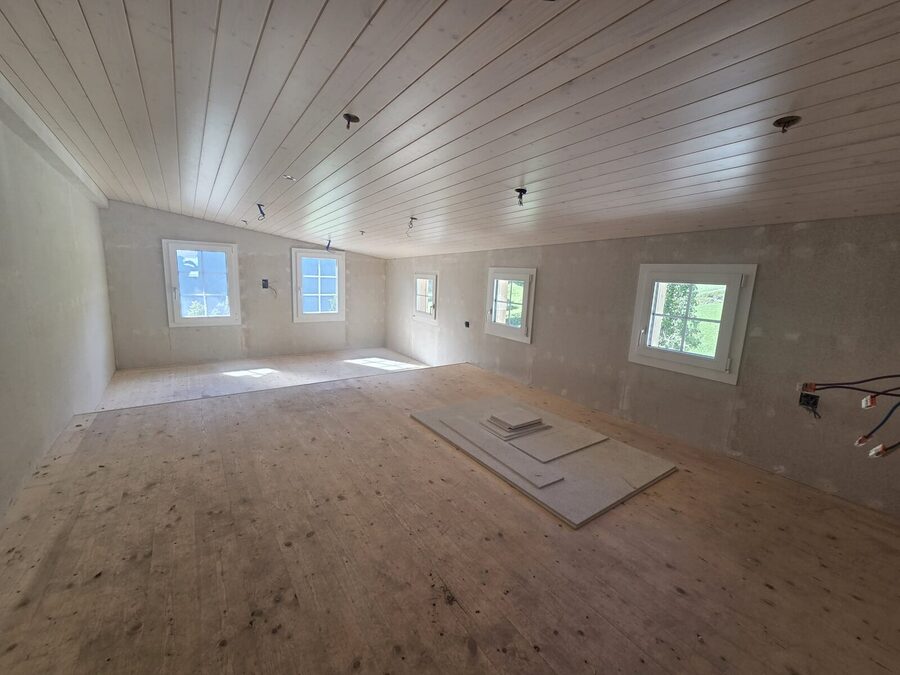 Ausgebauter Raum mit Holzdecke, verputzten Wänden und neuen Fenstern